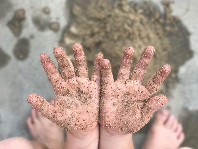 Childs hands in sand.